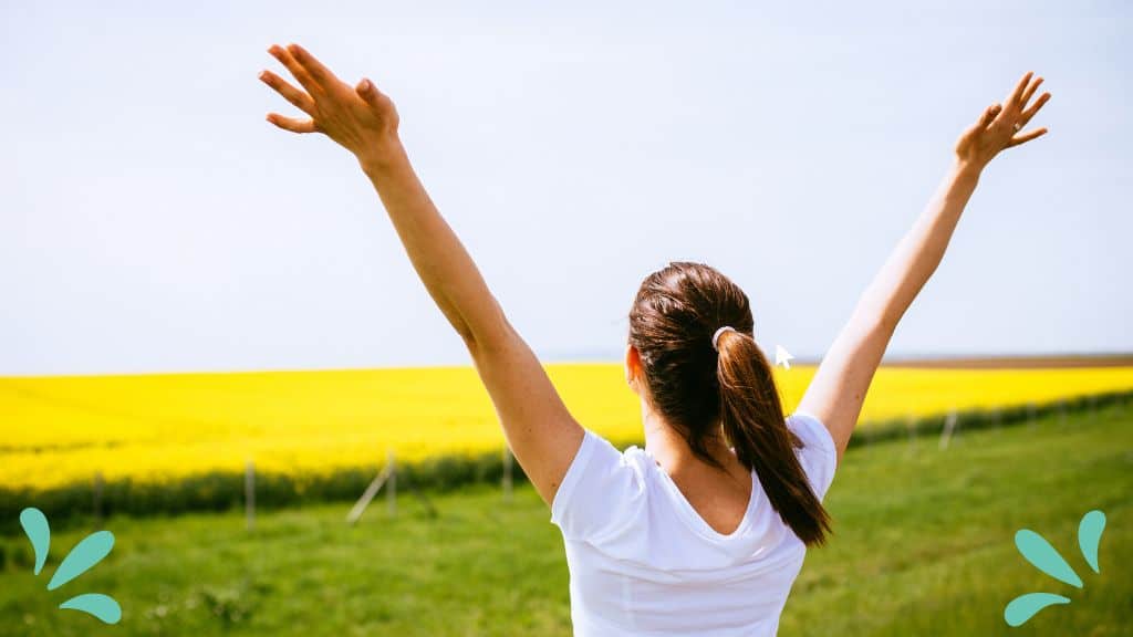 Woman standing in field with arms raised - for post 10 Bible Verses about Joy and Happiness
