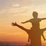 Bible verses about father's love at hope filled faith - silhouette of a boy sitting on his father's shoulders, standing in front of a sunset