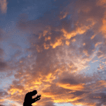 person praying in front of a sunset sky, for prayers for adult children, at Hope Filled Faith