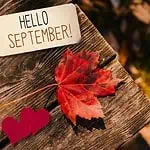 Hello september tag on a table with autumn leaves and red hearts