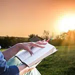 1 - woman reading Bible outdoors in front of sunrise - renewed by grace