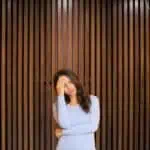 2 - woman holding forehead in front of a wooden wall - Bible verses for stress and hard times