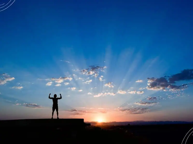 the Lord is my strength Bible verses - person standing on mountain with flexed arms