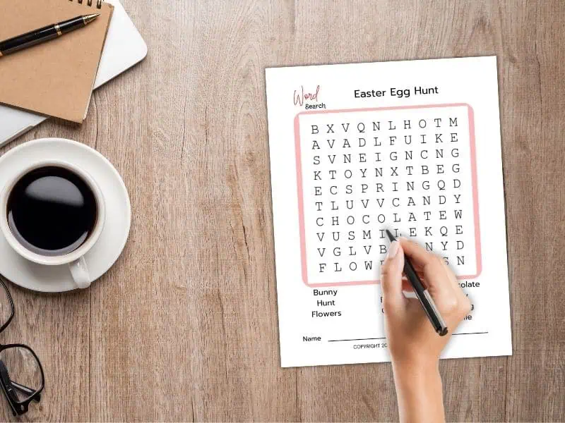 Easter word search printable - hand poised with pen over a word search on top of a desk